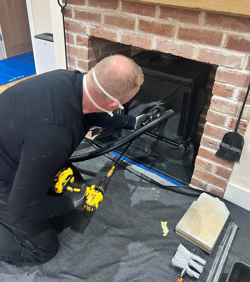 worker cleaning fireplace with vacuum and tools in home renovation setting